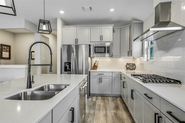 kitchen featuring wall chimney range hood, visible vents, a sink, stainless steel appliances, and light wood-style flooring