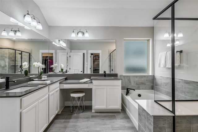full bath featuring a sink, a bath, a stall shower, and two vanities