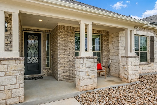 view of exterior entry featuring roof with shingles, covered porch, and stone siding
