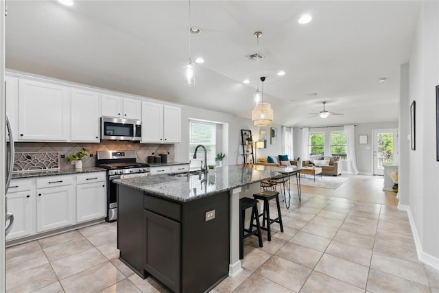 kitchen with appliances with stainless steel finishes, a sink, dark stone countertops, open floor plan, and backsplash