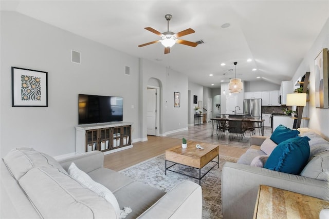 living room with light wood-style floors, arched walkways, a ceiling fan, lofted ceiling, and visible vents