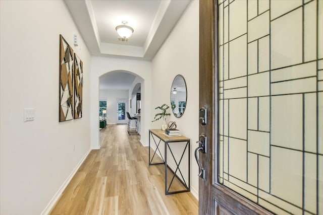 hall featuring a raised ceiling, arched walkways, baseboards, light wood-type flooring, and visible vents