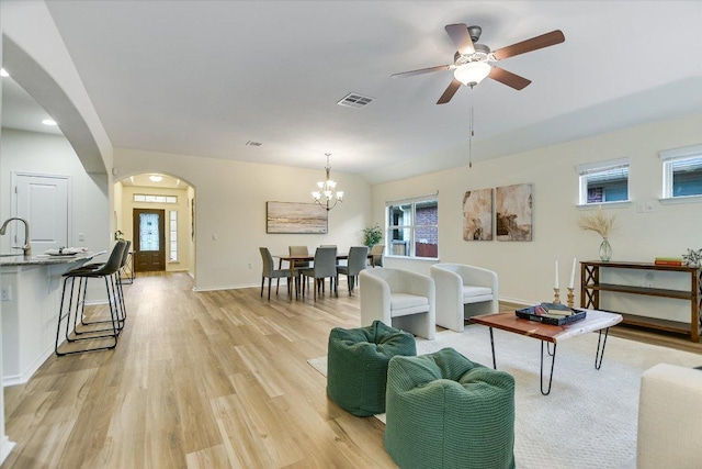 living area featuring visible vents, arched walkways, light wood-type flooring, baseboards, and ceiling fan with notable chandelier