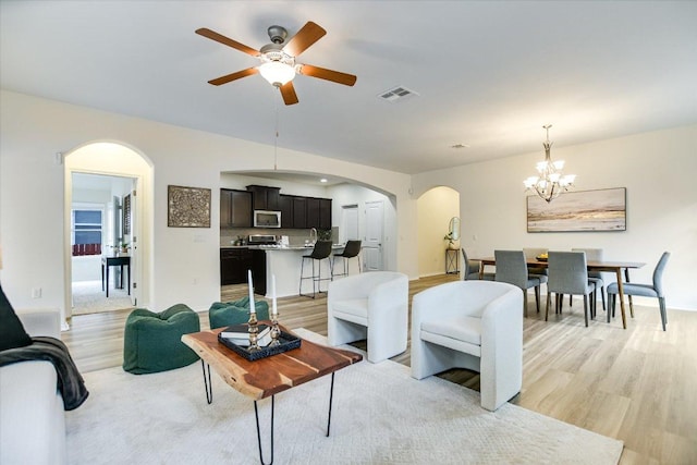 living room featuring arched walkways, visible vents, light wood finished floors, and ceiling fan with notable chandelier