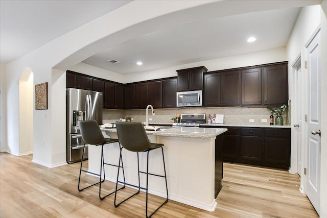 kitchen with decorative backsplash, a breakfast bar area, arched walkways, light wood-style floors, and stainless steel appliances
