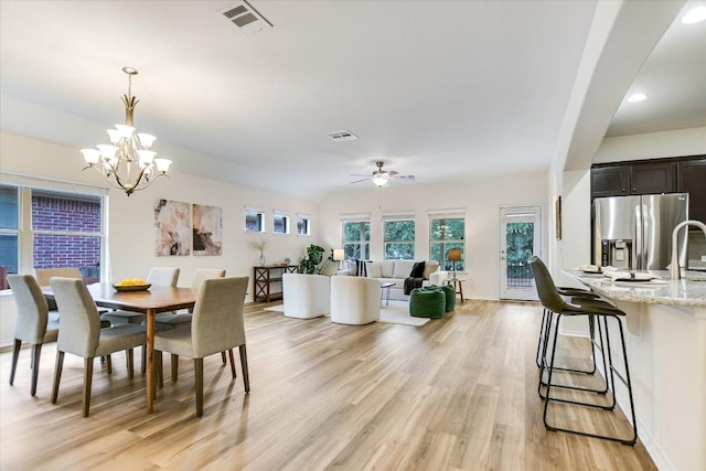 dining room with baseboards, ceiling fan with notable chandelier, light wood finished floors, and visible vents