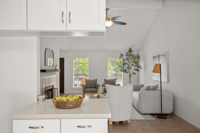 living area with tile patterned flooring, a fireplace, baseboards, a ceiling fan, and vaulted ceiling