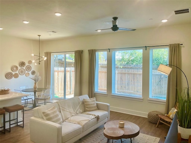 living room with visible vents, baseboards, ceiling fan with notable chandelier, and wood finished floors