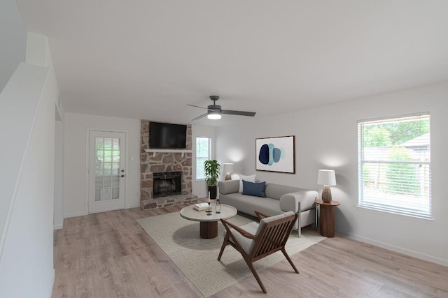 living area with light wood-style floors, baseboards, ceiling fan, and a stone fireplace