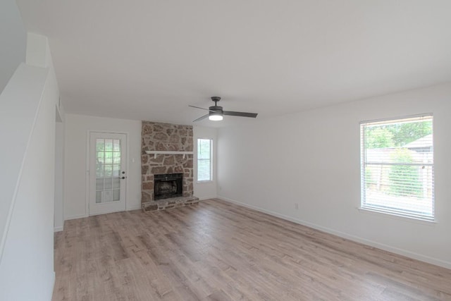 unfurnished living room featuring light wood-type flooring, a ceiling fan, baseboards, and a stone fireplace