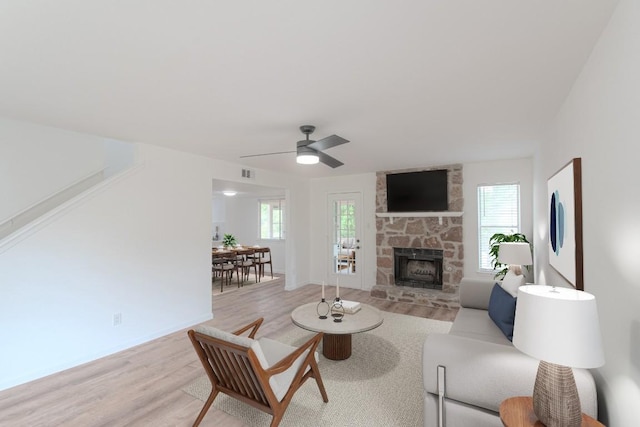 living area featuring ceiling fan, light wood finished floors, a stone fireplace, and a wealth of natural light