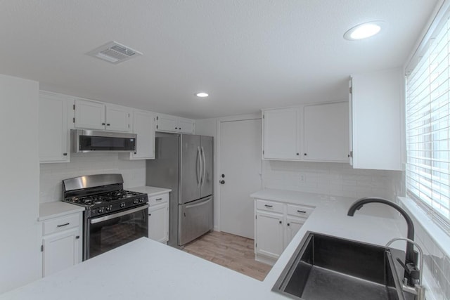 kitchen with visible vents, light wood-type flooring, a sink, white cabinets, and stainless steel appliances