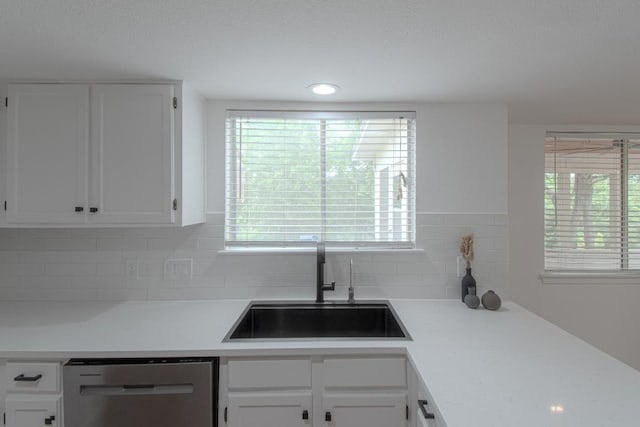 kitchen featuring stainless steel dishwasher, light countertops, white cabinets, a sink, and backsplash