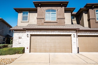 view of front of property featuring an attached garage, stone siding, and concrete driveway