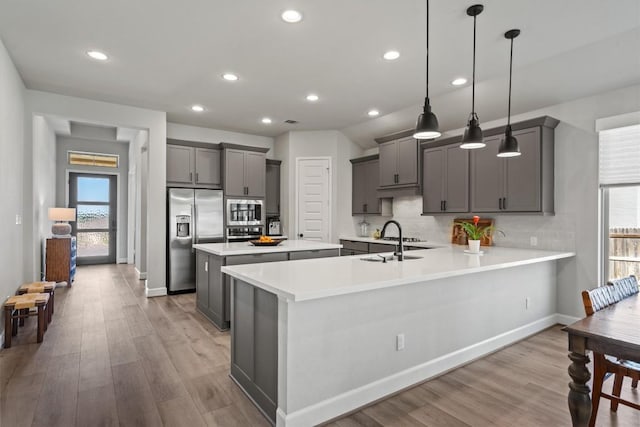 kitchen featuring light wood-style floors, a sink, appliances with stainless steel finishes, backsplash, and gray cabinetry