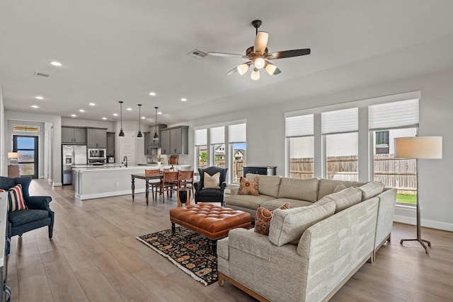 living area featuring light wood-style floors, a ceiling fan, and visible vents