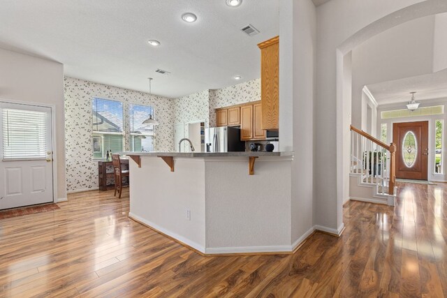 117 Summers Grn, Georgetown, TX 78633 - kitchen featuring arched walkways, stainless steel fridge, wallpapered walls, a kitchen bar, and light wood-type flooring