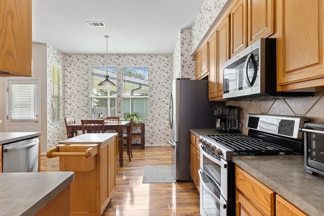 117 Summers Grn, Georgetown, TX 78633 - kitchen featuring stainless steel appliances, wallpapered walls, light wood-type flooring, baseboards, and pendant lighting