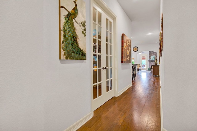 corridor featuring arched walkways, baseboards, french doors, and hardwood / wood-style flooring