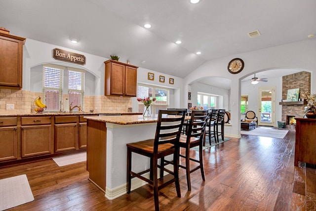 kitchen with brown cabinets, arched walkways, a ceiling fan, open floor plan, and dark wood-style floors