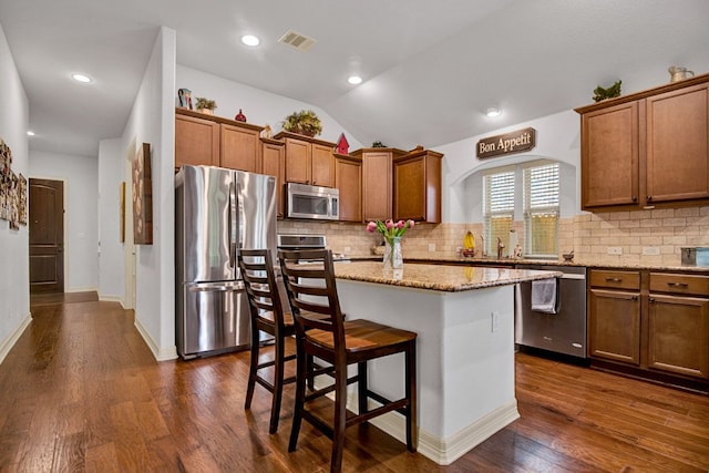 kitchen featuring decorative backsplash, a center island, brown cabinets, dark wood finished floors, and stainless steel appliances