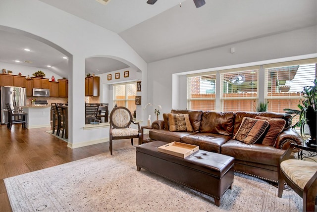 living area featuring a ceiling fan, arched walkways, wood finished floors, baseboards, and lofted ceiling