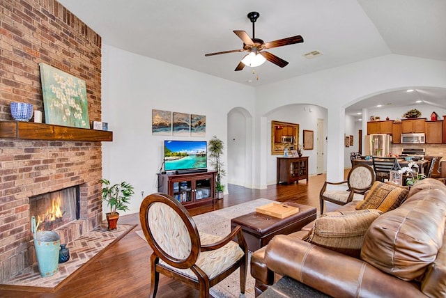 living room with visible vents, a ceiling fan, a brick fireplace, wood finished floors, and arched walkways