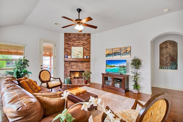 living area featuring ceiling fan, a brick fireplace, wood finished floors, and visible vents