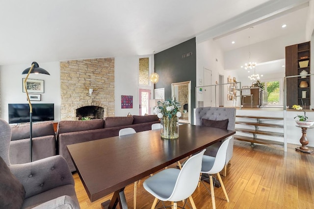 dining space featuring high vaulted ceiling, a notable chandelier, a stone fireplace, and light wood-type flooring