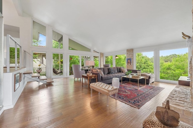 living area with high vaulted ceiling, a healthy amount of sunlight, and hardwood / wood-style flooring