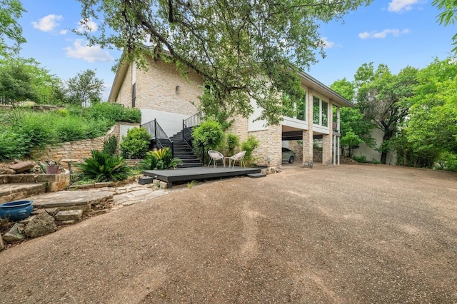 view of side of home featuring driveway, stone siding, stairway, and a carport
