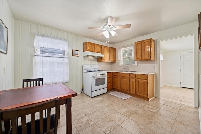 kitchen with a sink, light countertops, a ceiling fan, white range with gas stovetop, and under cabinet range hood