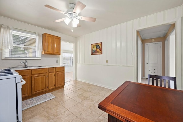 kitchen featuring white gas range, ceiling fan, brown cabinetry, light countertops, and a sink
