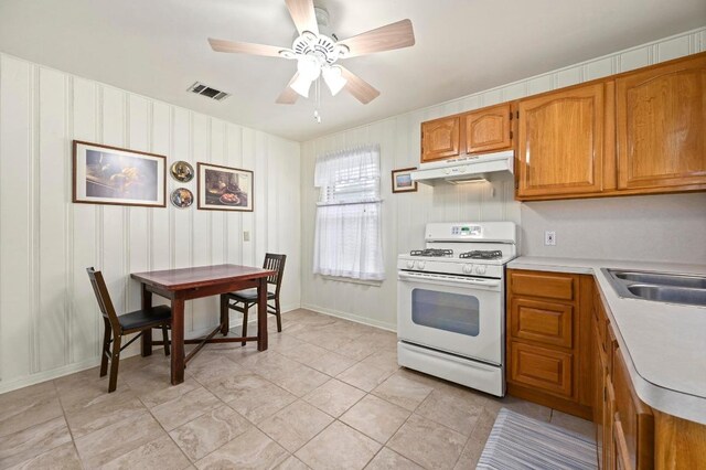 kitchen with light countertops, brown cabinetry, gas range gas stove, under cabinet range hood, and visible vents