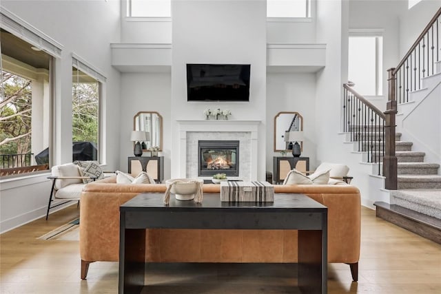 living area featuring light wood-style flooring, stairs, a glass covered fireplace, and a high ceiling