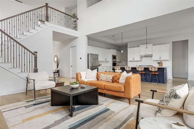 living room with stairs, baseboards, light wood-style flooring, and a high ceiling