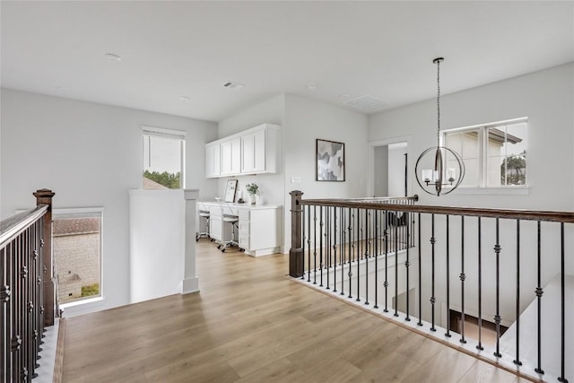 hall featuring an inviting chandelier, light wood finished floors, visible vents, and an upstairs landing