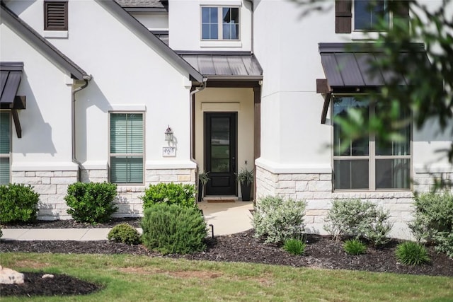 entrance to property with stucco siding, stone siding, and a standing seam roof