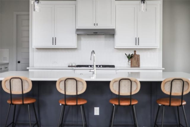 kitchen featuring a breakfast bar, light countertops, white cabinetry, under cabinet range hood, and tasteful backsplash