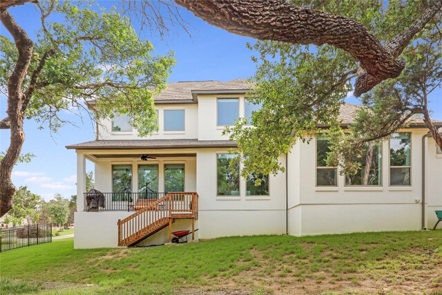 rear view of property with stucco siding, a porch, stairway, a ceiling fan, and a yard