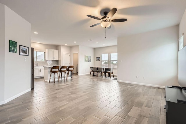 living room with ceiling fan, plenty of natural light, baseboards, and light wood finished floors