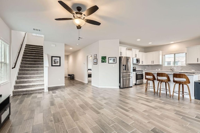 living room featuring visible vents, stairs, baseboards, a ceiling fan, and light wood finished floors