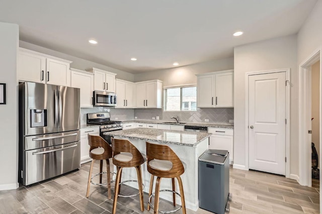 kitchen featuring a sink, stainless steel appliances, white cabinetry, wood tiled floor, and a kitchen island