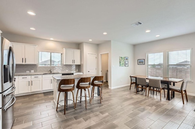 kitchen featuring a kitchen island, baseboards, stainless steel fridge, white cabinetry, and tasteful backsplash