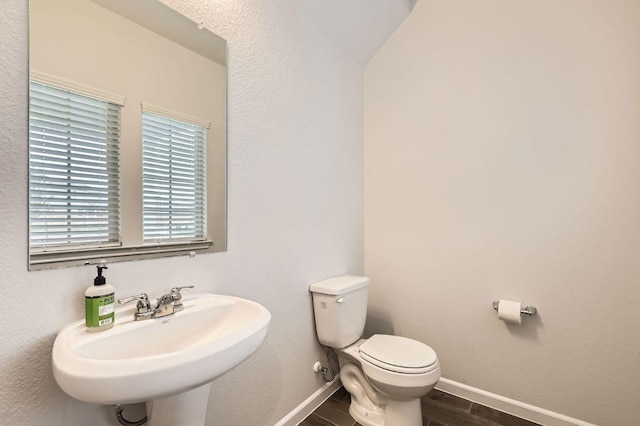 half bathroom featuring a sink, baseboards, toilet, and wood finished floors