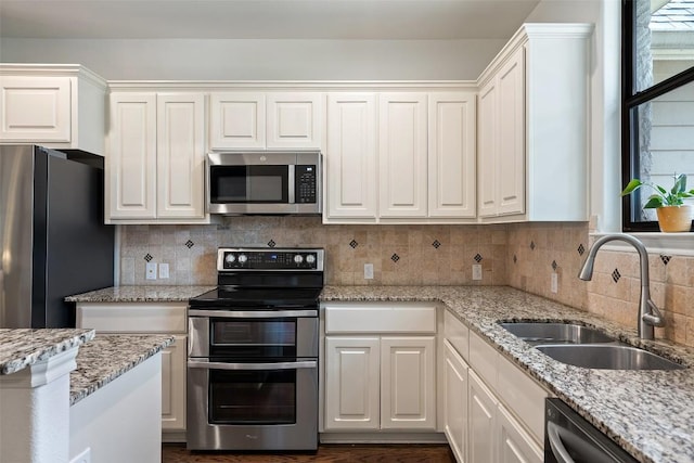kitchen featuring white cabinets, light stone counters, a sink, backsplash, and stainless steel appliances