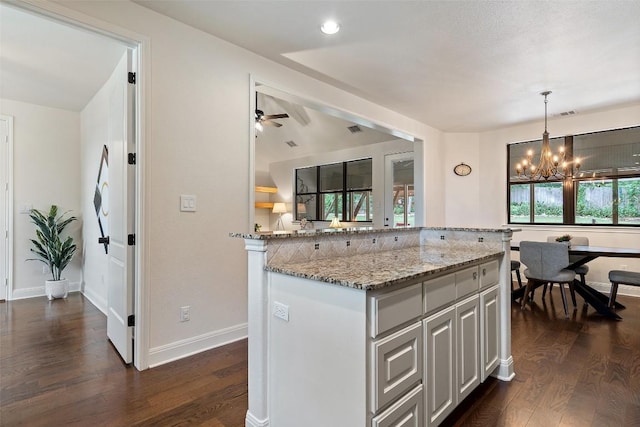 kitchen featuring dark wood-style flooring, light stone counters, hanging light fixtures, ceiling fan with notable chandelier, and a kitchen island