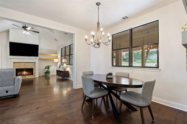 dining space featuring dark wood-style flooring, visible vents, baseboards, a warm lit fireplace, and lofted ceiling