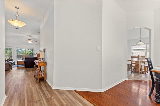 corridor featuring arched walkways, baseboards, and wood finished floors