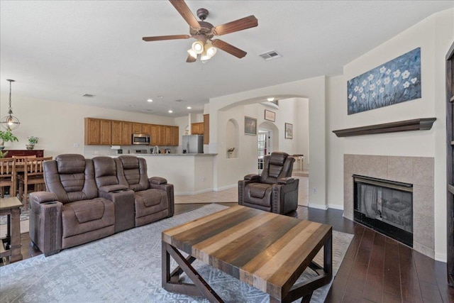 living area featuring a ceiling fan, visible vents, arched walkways, a fireplace, and wood-type flooring